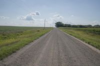 an empty dirt road stretches into the distance with power lines in the foreground under a blue sky