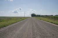 an empty dirt road stretches into the distance with power lines in the foreground under a blue sky