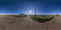 a fish - eye lens shot of an empty dirt road and field in the background