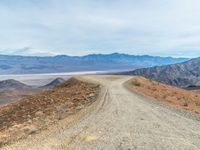 an empty dirt road leading to the mountains, with a very wide view of mountains