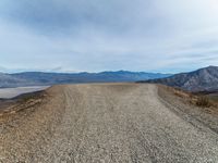 an empty dirt road with mountains in the background and a few clouds over the horizon