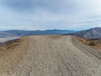 an empty dirt road with mountains in the background and a few clouds over the horizon