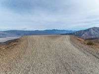 an empty dirt road with mountains in the background and a few clouds over the horizon