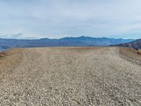 an empty dirt road with mountains in the background and a few clouds over the horizon