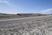 a dirt road is surrounded by some hills and desert like terrain as the vehicle sits on it