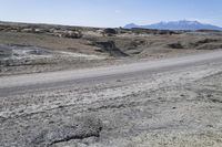 a dirt road is surrounded by some hills and desert like terrain as the vehicle sits on it