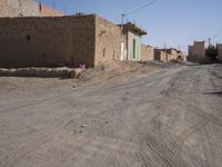 an empty dirt road through a town near a building wall, and buildings along side