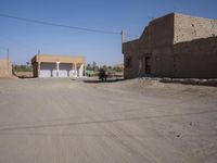 an empty dirt road through a town near a building wall, and buildings along side