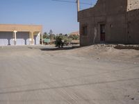an empty dirt road through a town near a building wall, and buildings along side