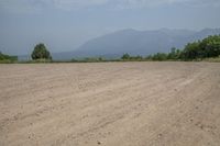 there is an empty dirt road near trees and mountains behind it, as well as the ocean