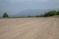 there is an empty dirt road near trees and mountains behind it, as well as the ocean