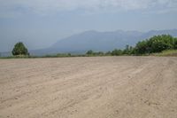 there is an empty dirt road near trees and mountains behind it, as well as the ocean