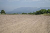 there is an empty dirt road near trees and mountains behind it, as well as the ocean