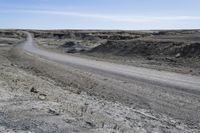 a dirt road is surrounded by some hills and desert like terrain as the vehicle sits on it