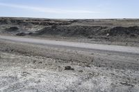 a dirt road is surrounded by some hills and desert like terrain as the vehicle sits on it