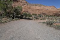 an empty dirt road in the desert with a house and trees by it with no people