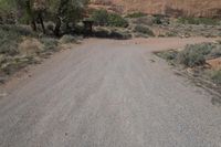 an empty dirt road in the desert with a house and trees by it with no people