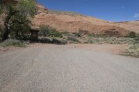 an empty dirt road in the desert with a house and trees by it with no people