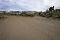 an empty dirt road runs through the desert and has small shrubbery and bushes in the distance