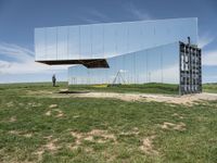 an empty field is set under mirrored structures and people are standing in the grass near them