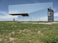 an empty field is set under mirrored structures and people are standing in the grass near them