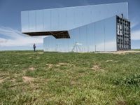 an empty field is set under mirrored structures and people are standing in the grass near them