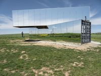 an empty field is set under mirrored structures and people are standing in the grass near them