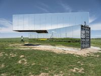 an empty field is set under mirrored structures and people are standing in the grass near them