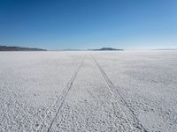 the tracks of a person walking across a large empty field of snow and mountains in the distance