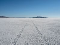 the tracks of a person walking across a large empty field of snow and mountains in the distance