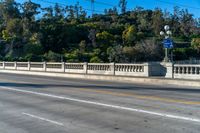 an empty freeway passes by a bridge with lots of trees behind it and two streetlights