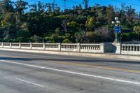 an empty freeway passes by a bridge with lots of trees behind it and two streetlights