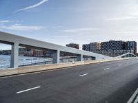 a very wide and empty freeway near some buildings and water and a large bridge that is over looking the city