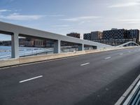 a very wide and empty freeway near some buildings and water and a large bridge that is over looking the city