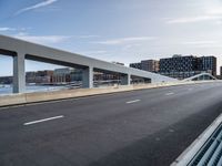 a very wide and empty freeway near some buildings and water and a large bridge that is over looking the city