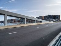 a very wide and empty freeway near some buildings and water and a large bridge that is over looking the city