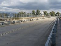 long empty freeway with metal fence on both sides and sky with clouds overhead, near city with buildings