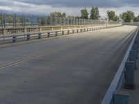 long empty freeway with metal fence on both sides and sky with clouds overhead, near city with buildings