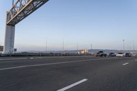 several cars drive on an empty freeway under a suspension bridge in the morning sun setting