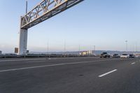 several cars drive on an empty freeway under a suspension bridge in the morning sun setting