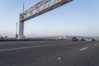 several cars drive on an empty freeway under a suspension bridge in the morning sun setting