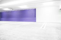 an empty car parking garage with purple wall and white floors with markings on the floor