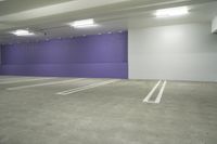 an empty car parking garage with purple wall and white floors with markings on the floor