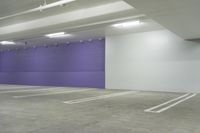 an empty car parking garage with purple wall and white floors with markings on the floor