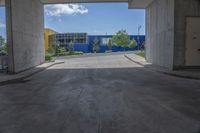 an empty garage with lots of blue walls and trees growing outside of it, and a large blue structure in the background