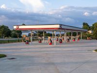 an empty gas station sitting on top of a road next to a lush green hillside