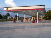 an empty gas station sitting on top of a road next to a lush green hillside