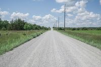an empty gravel road is on one side and a sky line across the other from the telephone poles