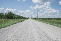 an empty gravel road is on one side and a sky line across the other from the telephone poles