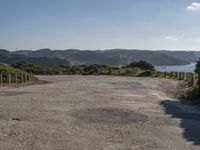 an empty gravel road winding down a hillside with green hills in the background and water on either side